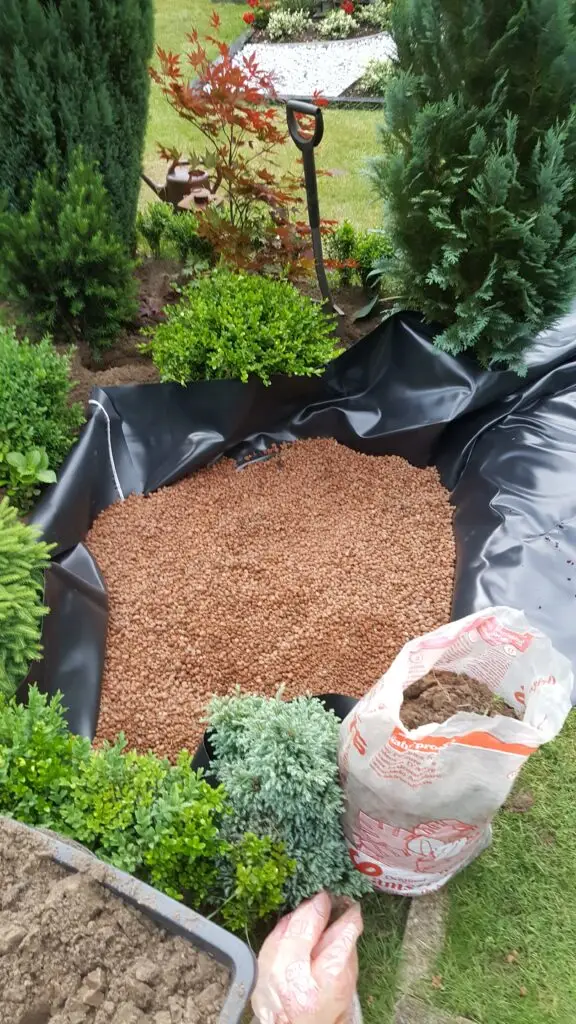 Foto von einem Grab, bei dem ein Teil ausgehoben wurde, mit Teichfolie ausgelegt ist und Bläton auf der Teichfolie geschüttet wurde.