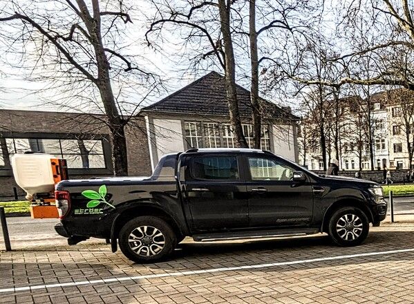 Foto von einem Ford Ranger Wildtrack mit Firmenbeschriftung von der Firma Ströer Innen- und Außengrün. An der Heckklappe ist ein Salzstreuer befestigt.