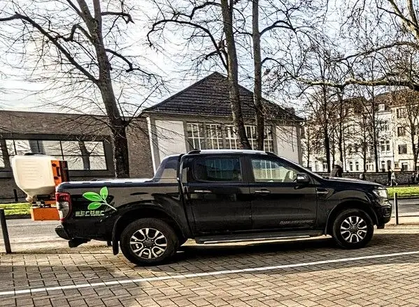Foto von einem Ford Ranger Wildtrack mit Firmenbeschriftung von der Firma Ströer Innen- und Außengrün. An der Heckklappe ist ein Salzstreuer befestigt.