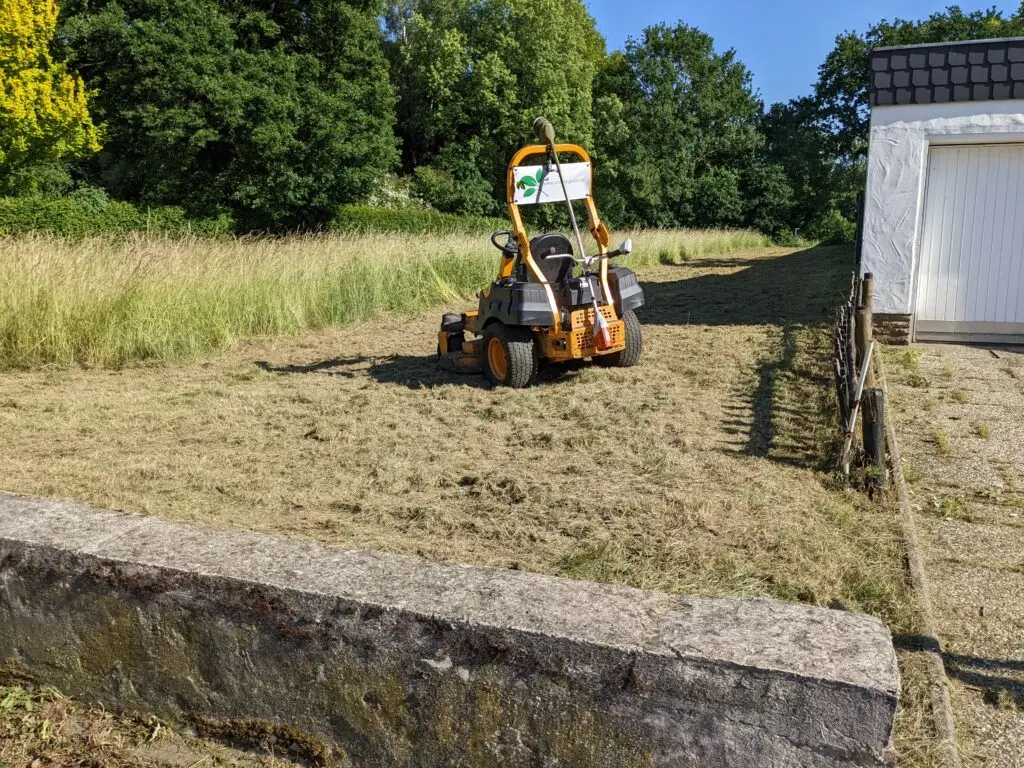 Foto von einem Aufsitzrasenmäher auf einer Wiese, die zum Teil gemäht ist.