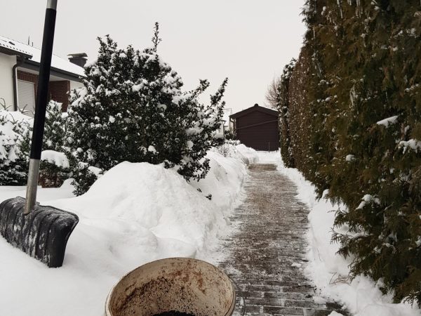 Foto von einem Eimer Splitt, einer Schneeschaufel und einem Gehweg der von Schnee befreit und abgestreut wurde.